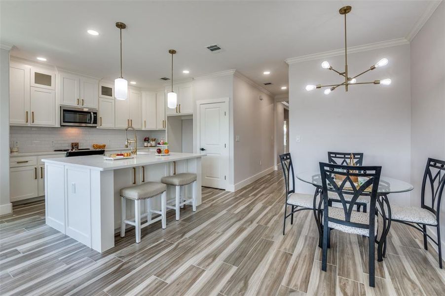 Kitchen featuring backsplash, white cabinetry, crown molding, a kitchen island with sink, and hanging light fixtures