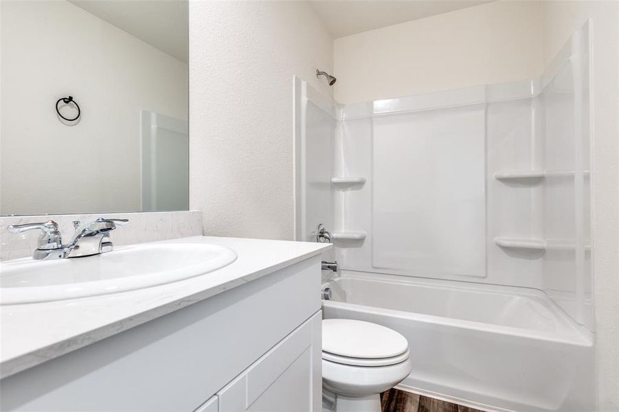 Full bathroom with washtub / shower combination, vanity, dark wood-style floors, and a textured wall