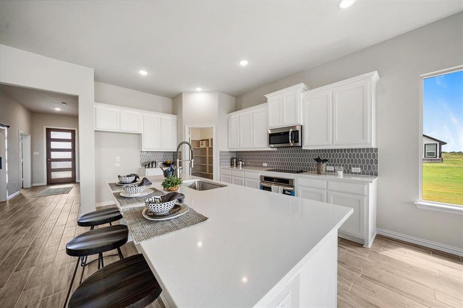 Kitchen featuring a breakfast bar area, white cabinets, wood finish floors, decorative backsplash, and recessed lighting Kitchen featuring a breakfast bar area, white cabinets, wood finish floors, decorative backsplash, and recessed lighting