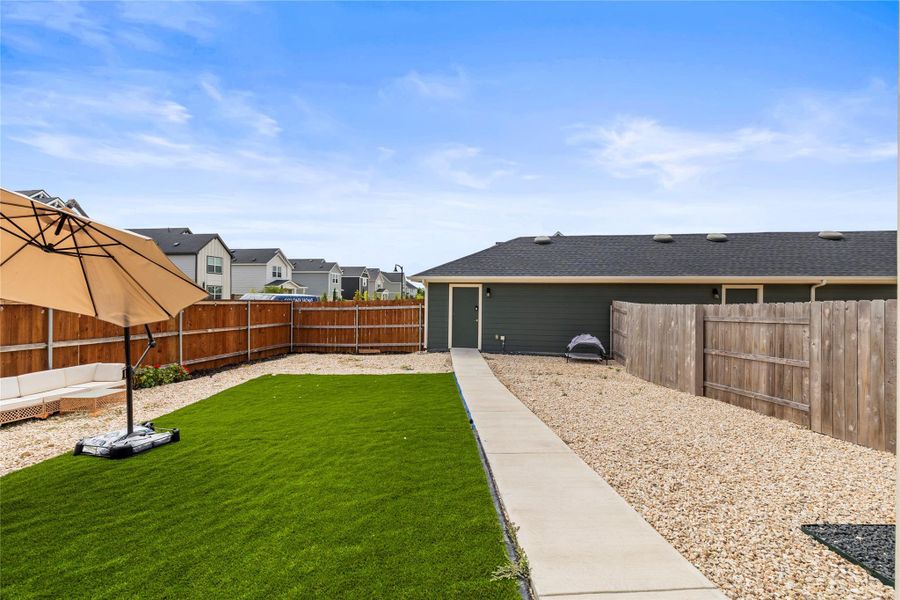 A fenced backyard offers a low-maintenance artificial turf area and a concrete pathway leading to the homes rear entrance and two car garage.