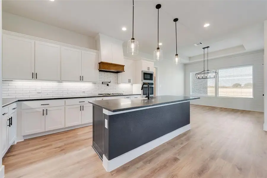 Spacious kitchen featuring an expansive center island, white shaker-style cabinetry with matte black hardware, white subway tile backsplash, and wood-finish flooring