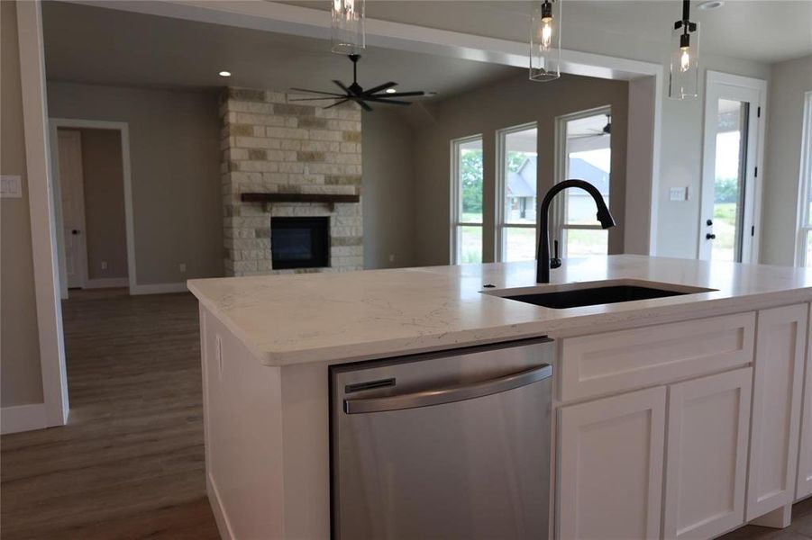 Kitchen with pendant lighting, an island with sink, dark hardwood / wood-style floors, stainless steel dishwasher, and a stone fireplace