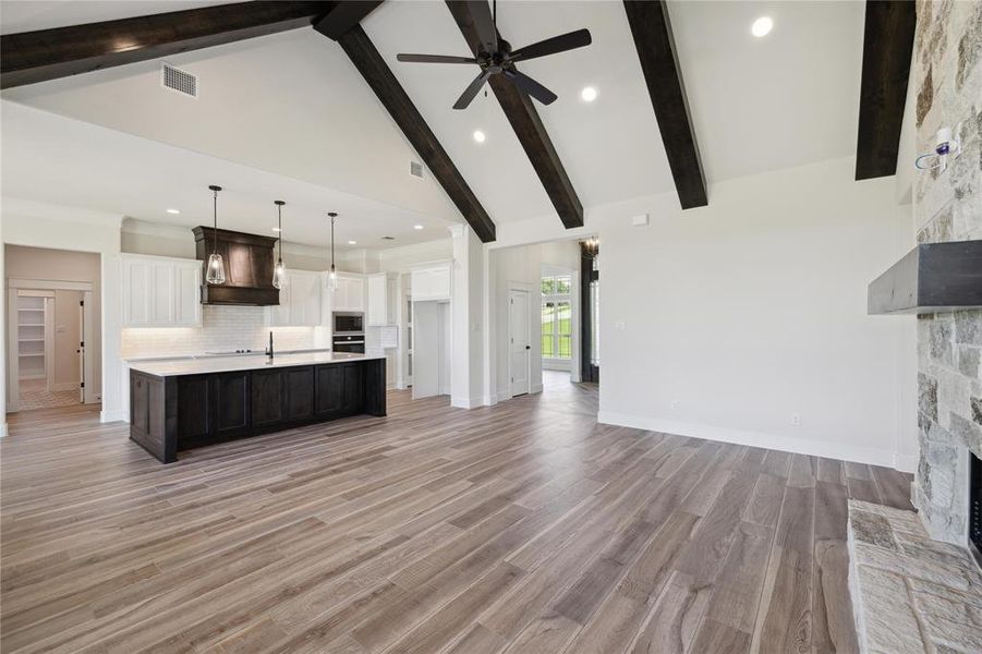 Kitchen featuring a fireplace, pendant lighting, high vaulted ceiling, an island with sink, and beamed ceiling