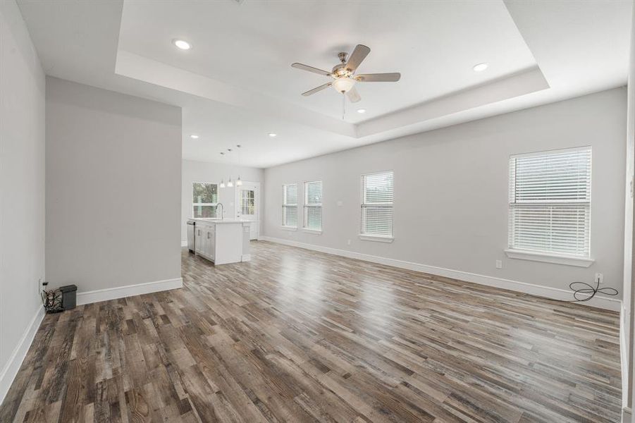 Unfurnished living room with a tray ceiling, light wood-type flooring, a ceiling fan, and recessed lighting Unfurnished living room with a tray ceiling, light wood-type flooring, a ceiling fan, and recessed lighting