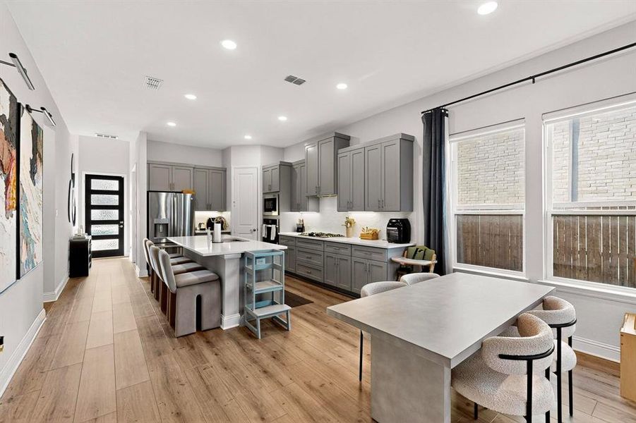 Kitchen with a breakfast bar area, a kitchen island with sink, recessed lighting, light wood finished floors, and gray cabinetry Kitchen with a breakfast bar area, a kitchen island with sink, recessed lighting, light wood finished floors, and gray cabinetry