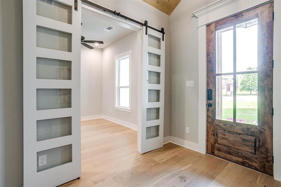 Doorway featuring light wood-style flooring, a barn door, baseboards, visible vents, and ceiling fan Doorway featuring light wood-style flooring, a barn door, baseboards, visible vents, and ceiling fan