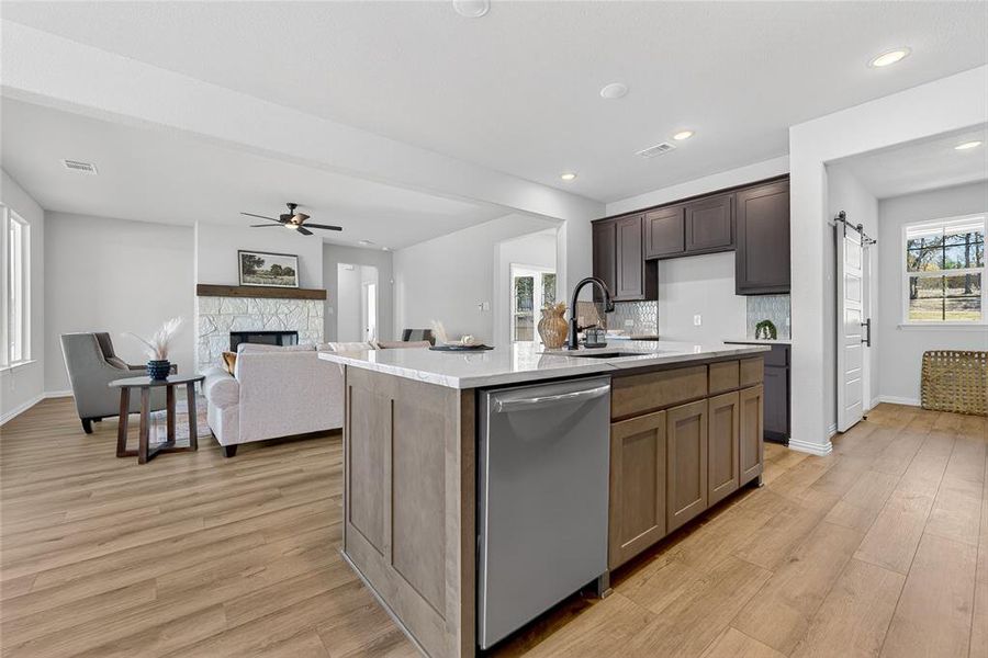 Kitchen with light stone counters, stainless steel dishwasher, light wood-type flooring, a stone fireplace, and recessed lighting Kitchen with light stone counters, stainless steel dishwasher, light wood-type flooring, a stone fireplace, and recessed lighting