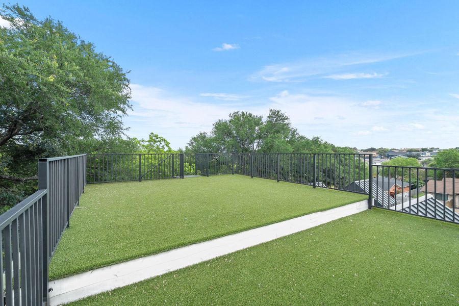 Rooftop patio featuring expansive artificial turf, modern black metal railing, and concrete border