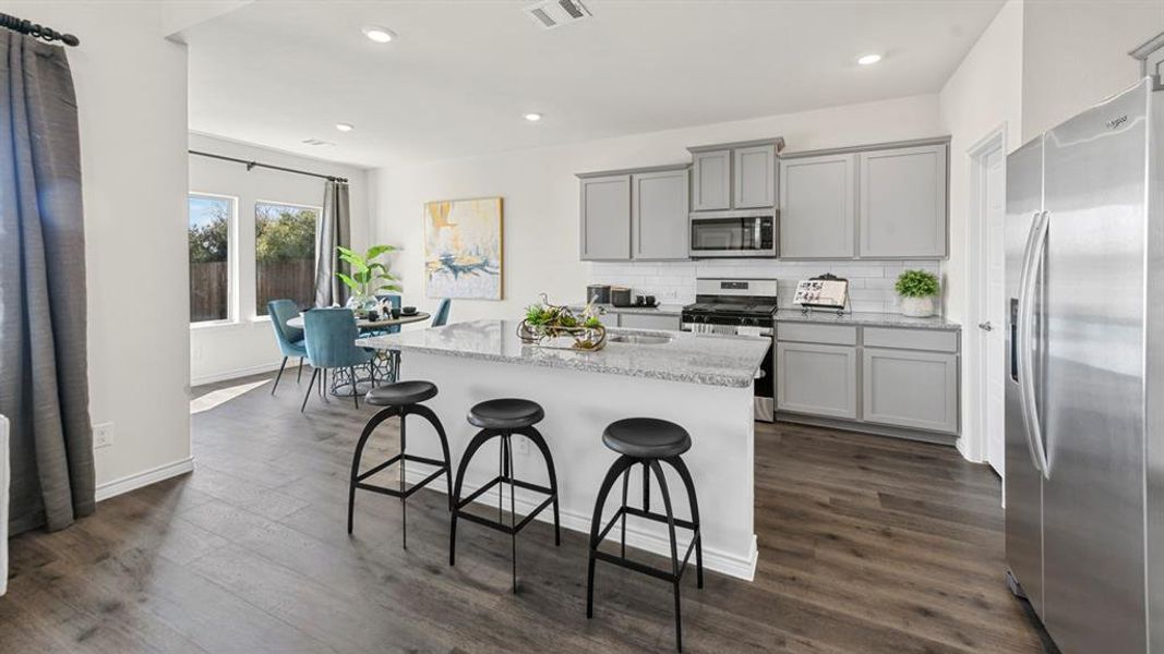 Kitchen featuring a large central island with a granite countertop, gray shaker-style cabinetry, stainless steel appliances, and a subway tile backsplash