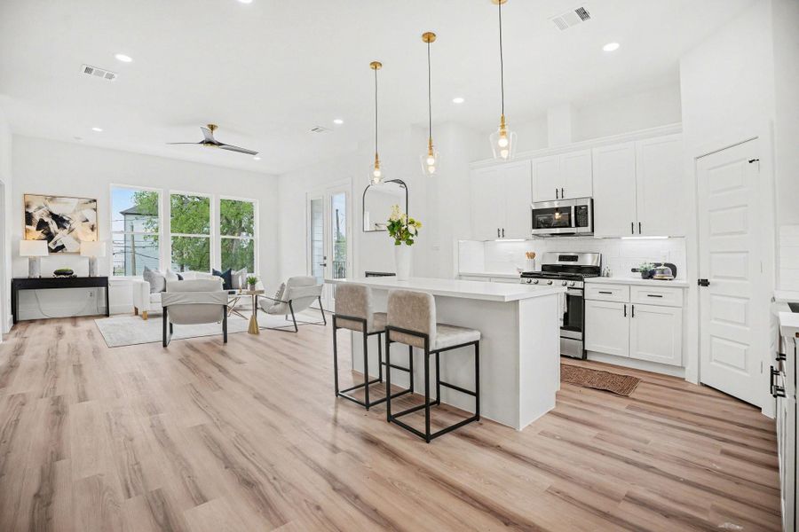 Bright, open-concept kitchen and living area with modern finishes. Features include sleek white cabinetry, stainless steel appliances, pendant lighting, and large windows offering natural light and views. Perfect for entertaining.