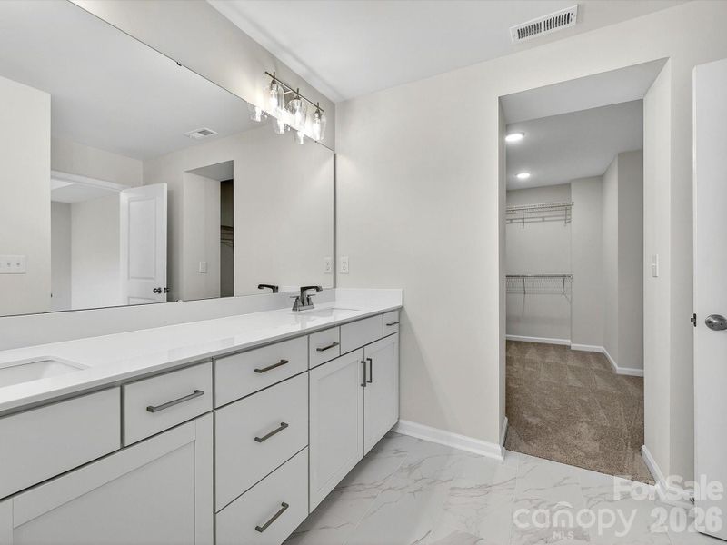 owners bath with oversized dual vanity, with soft close doors and drawers, quartz countertops leading to large primary closet