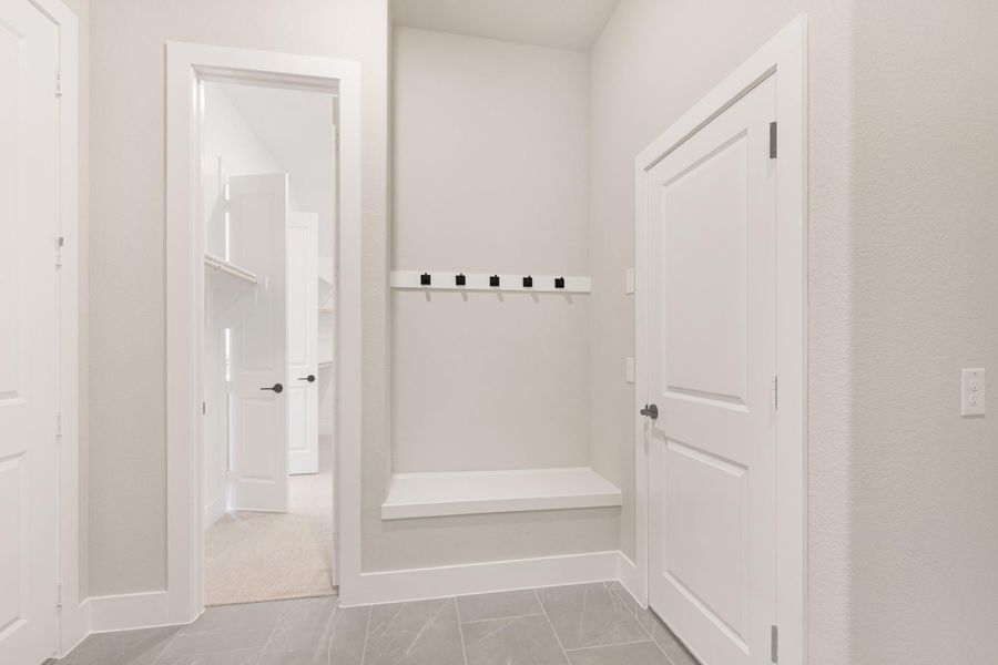 Mudroom with built-in bench, coat hooks, and tile floors with view into closet area