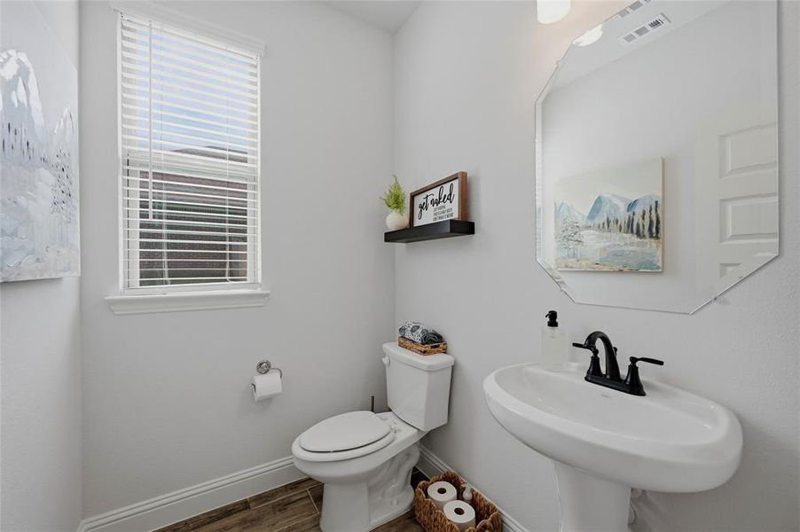 Pedestal sink with matte black faucet, wall-mounted octagonal mirror, and wood-finish flooring