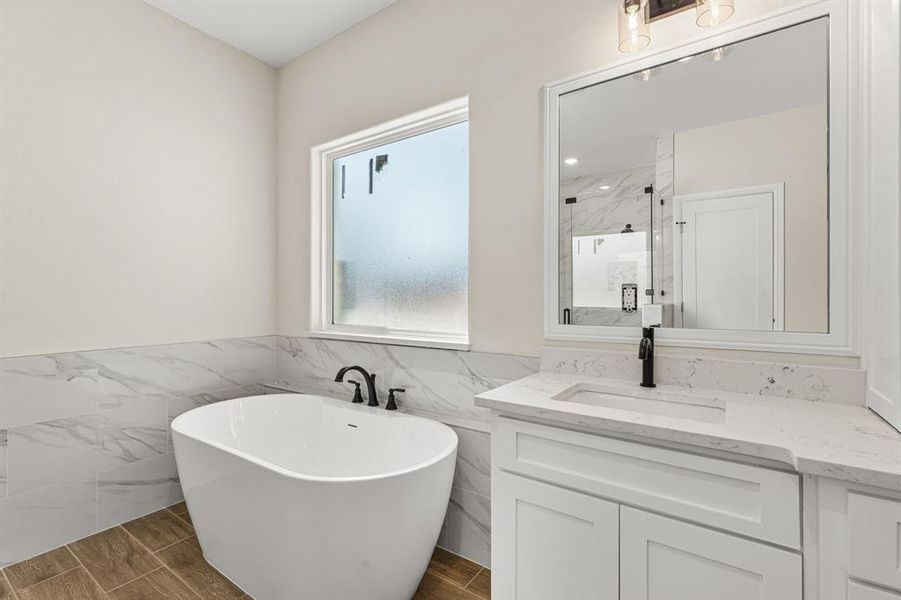 Bathroom with wood finish floors, a soaking tub, vanity, tile walls, and a marble finish shower