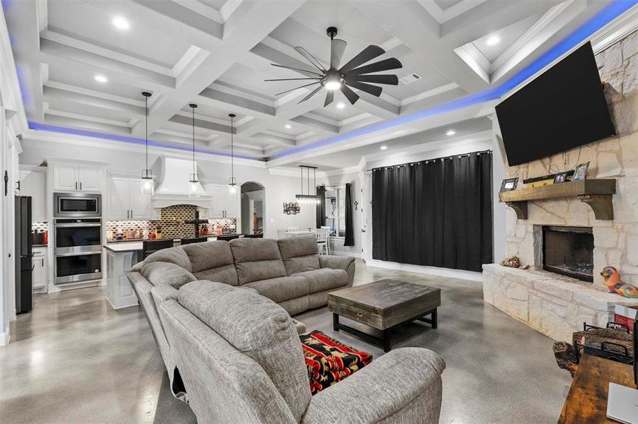 Living room with beam ceiling, coffered ceiling, a fireplace, and ceiling fan