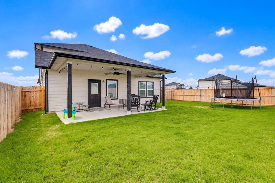 Spacious backyard featuring a covered patio with a ceiling fan, string lighting, and a concrete slab