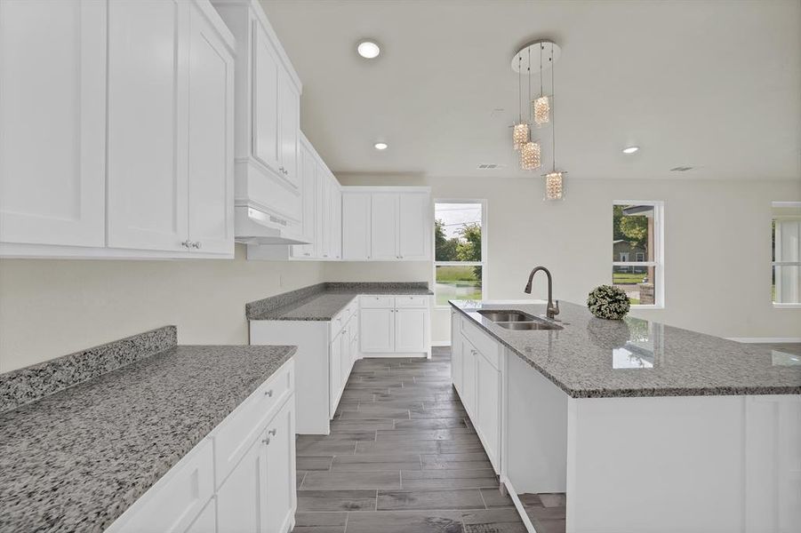 Kitchen featuring light stone countertops, recessed lighting, an island with sink, white cabinetry, and hanging light fixtures