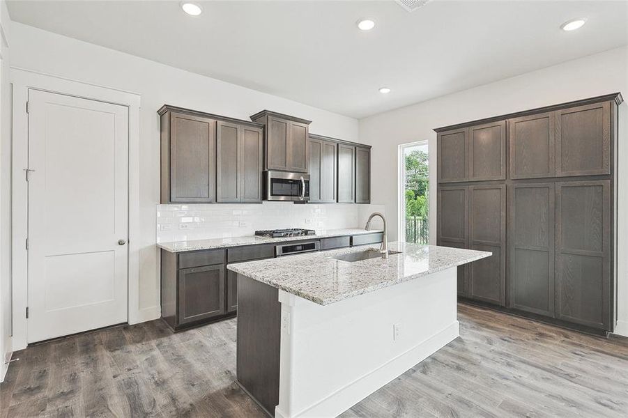 Kitchen featuring sink, appliances with stainless steel finishes, hardwood / wood-style floors, light stone counters, and an island with sink