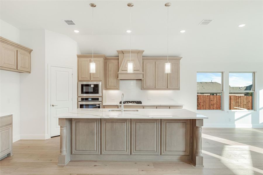 Kitchen with large center island, light wood cabinets, white countertops, and stainless steel appliances