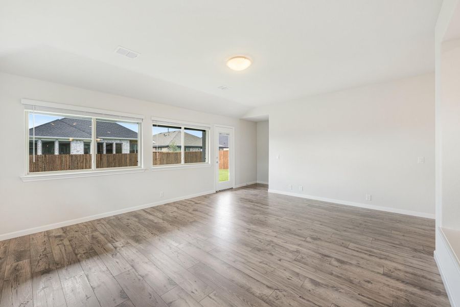 Empty living room with light wood floors, white walls, and large windows overlooking backyard