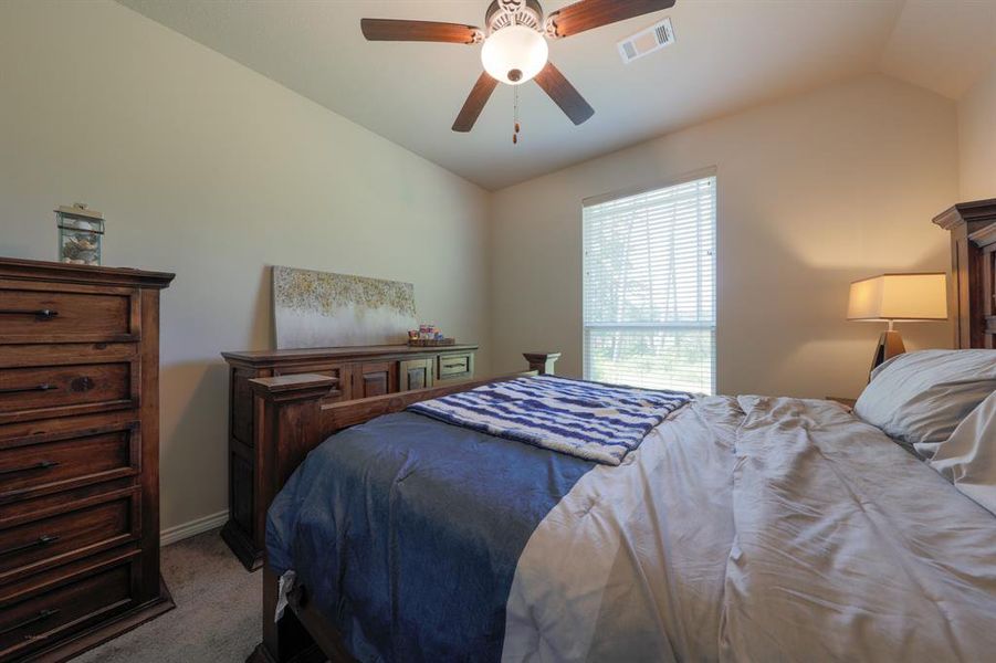 Cozy bedroom with warm, wooden furniture, a large window allowing natural light, and a ceiling fan. The space feels inviting and functional, perfect for relaxation.