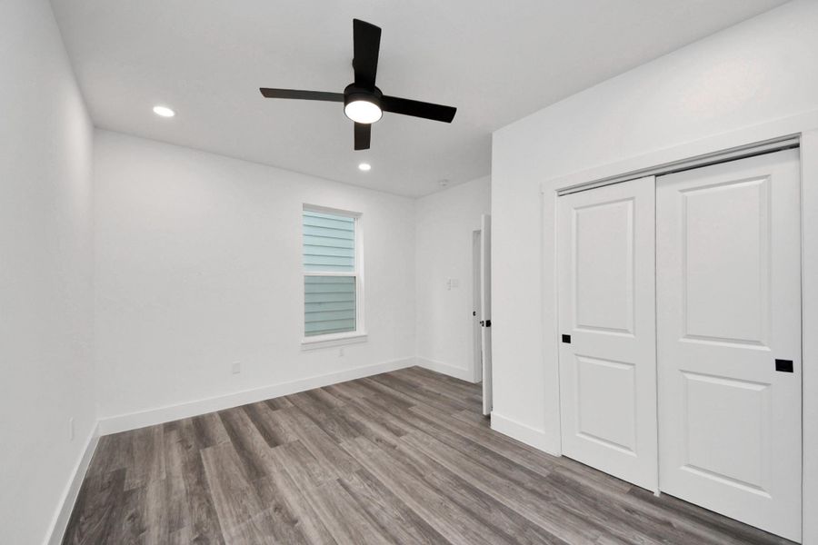 This room features sleek wood flooring, a ceiling fan, recessed lighting, and a window for natural light. It includes a closet with sliding doors, offering ample storage in a bright and modern space. This room features sleek wood flooring, a ceiling fan, recessed lighting, and a window for natural light. It includes a closet with sliding doors, offering ample storage in a bright and modern space.