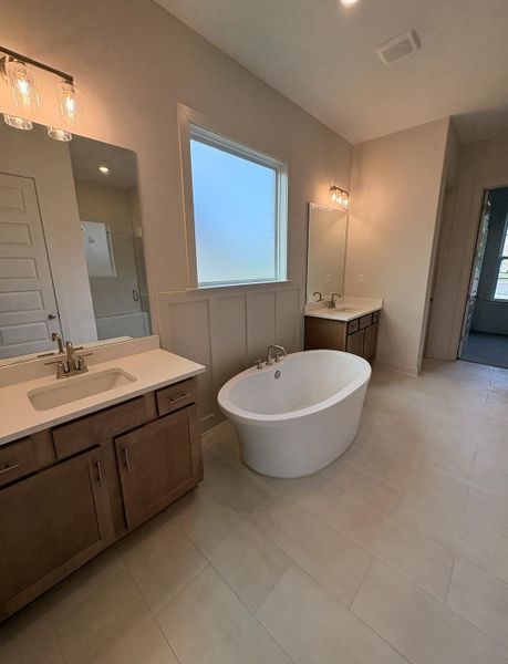 Freestanding soaking tub centered in a spacious bathroom featuring dual vanity cabinets with undermount sinks and light-toned countertops