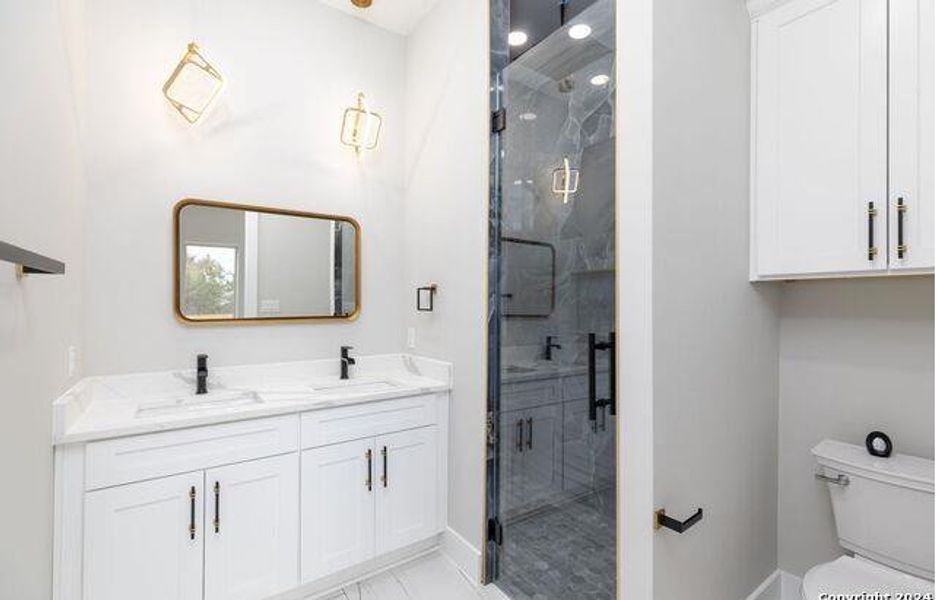 Double vanity with white cabinetry and integrated sinks, complemented by a gold-framed mirror and geometric sconces