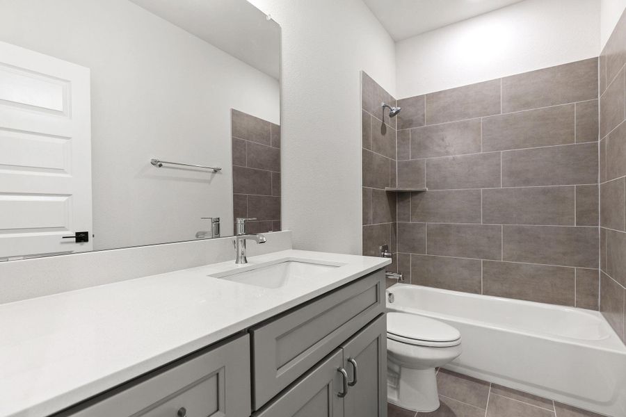A well-lit bathroom features a vanity with sleek counters, complementing the tiled tub and shower combination. A well-lit bathroom features a vanity with sleek counters, complementing the tiled tub and shower combination.