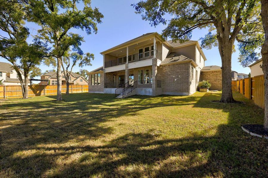 Rear view of house featuring a balcony, a fenced backyard, brick siding, and a patio area
