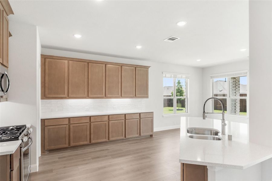 Kitchen with brown wood cabinets, white quartz island with sink, and light hardwood floors