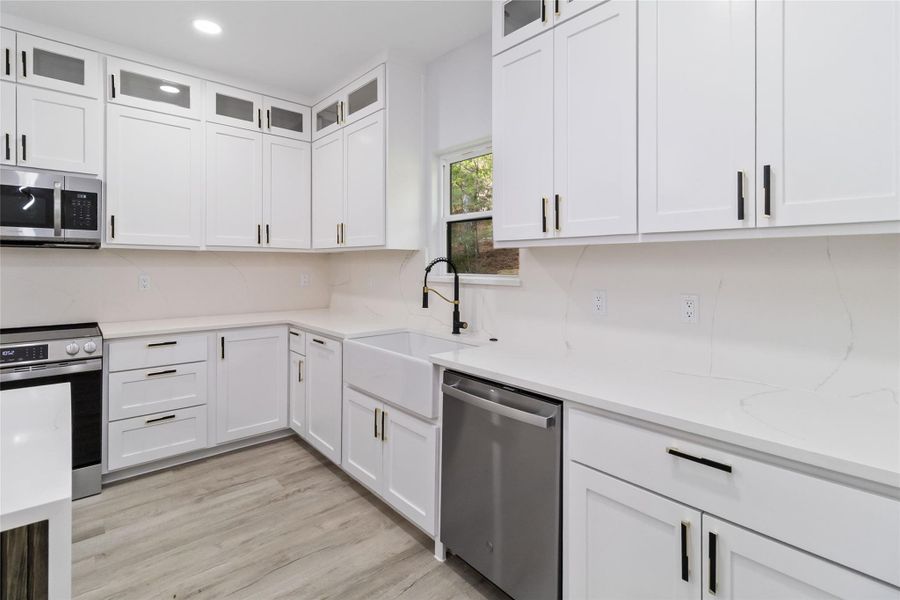 Kitchen featuring glass insert cabinets, stainless steel appliances, white cabinetry, light stone countertops, and recessed lighting