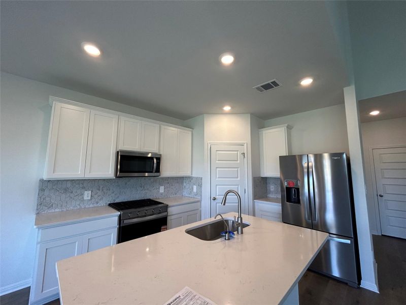 Kitchen featuring stainless steel appliances, backsplash, white cabinetry, a kitchen island with sink, and light stone countertops Kitchen featuring stainless steel appliances, backsplash, white cabinetry, a kitchen island with sink, and light stone countertops