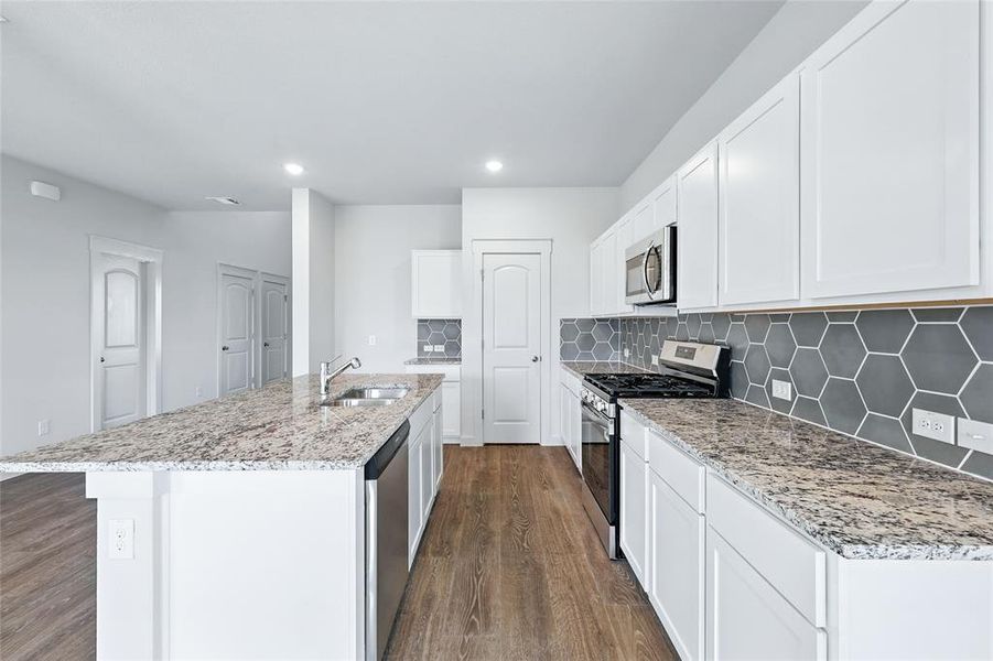 Kitchen featuring appliances with stainless steel finishes, backsplash, dark wood-style floors, a center island with sink, and white cabinets Kitchen featuring appliances with stainless steel finishes, backsplash, dark wood-style floors, a center island with sink, and white cabinets