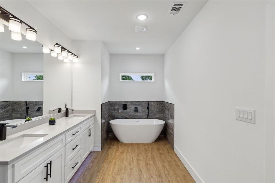 Bathroom with double vanity, tile walls, wood-type flooring, and a tub