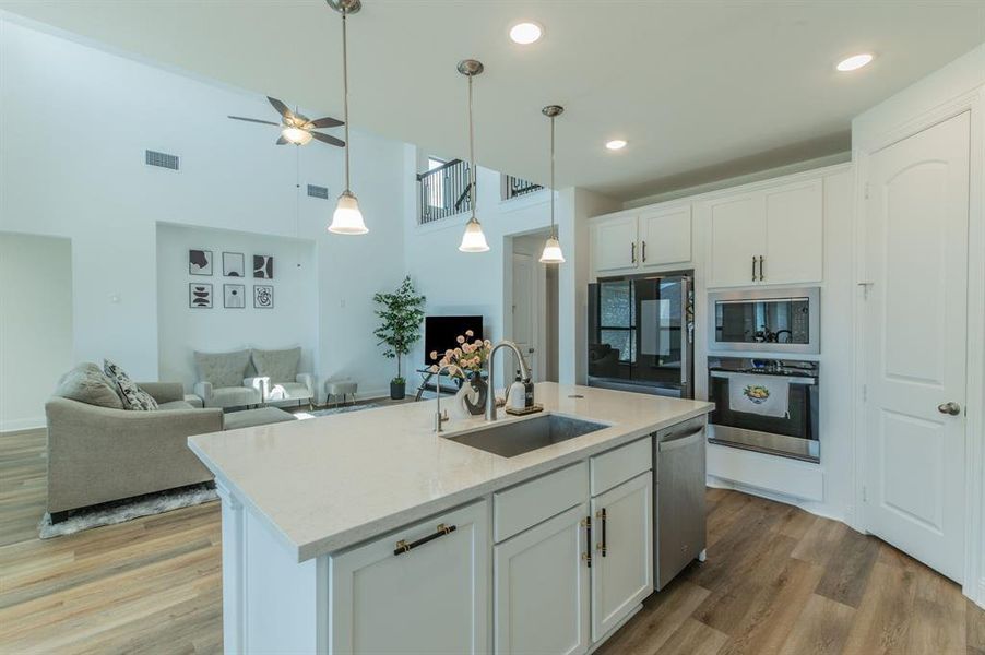 Open-concept kitchen featuring a central island with an undermount sink, pendant lighting, stainless steel appliances, and white cabinetry