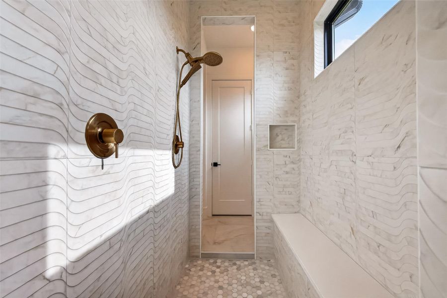A Texas-sized fully tiled walk-through shower complete with gold hardware, bench seating, and natural lighting!