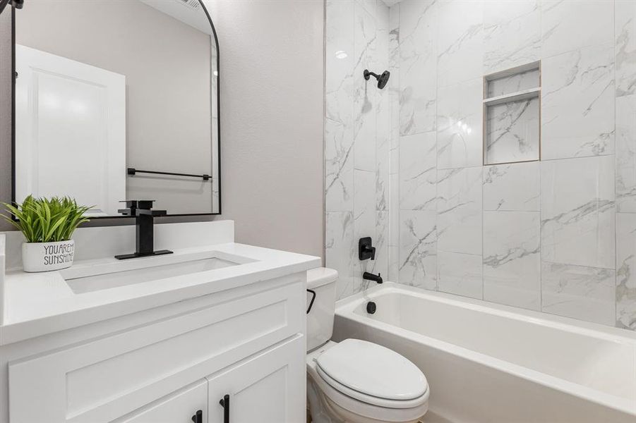 Full bathroom featuring vanity, tiled shower / bath combo, and toilet