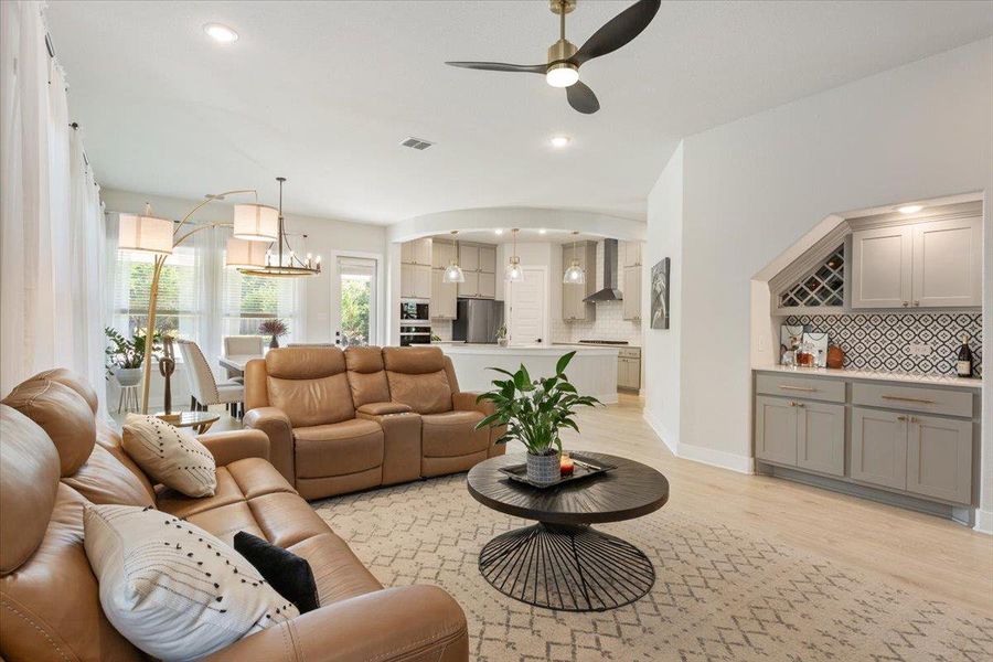 Living room featuring ceiling fan, light wood-style flooring, suspended lighting, and arched walkways