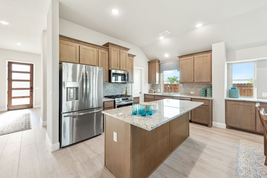 Kitchen with brown cabinets, granite island, stainless steel appliances, and light hardwood floors Kitchen with brown cabinets, granite island, stainless steel appliances, and light hardwood floors