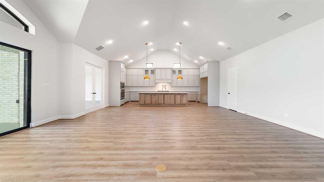 Unfurnished living room featuring plenty of natural light, high vaulted ceiling, sink, and light hardwood / wood-style floors