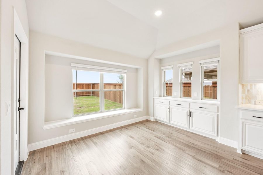Empty dining area with light wood floors, white built-in cabinets, and large windows overlooking a fenced backyard Empty dining area with light wood floors, white built-in cabinets, and large windows overlooking a fenced backyard