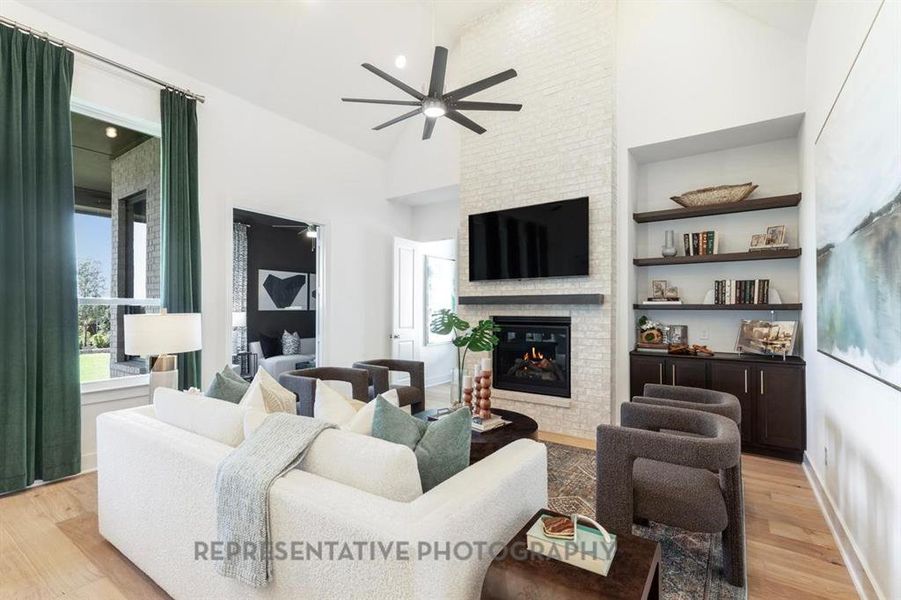 Living area featuring light wood-style flooring, high vaulted ceiling, a ceiling fan, a fireplace, and built in features