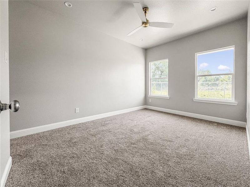 Room featuring neutral gray walls, plush gray carpet, a ceiling fan with integrated lighting, and two double-hung windows Room featuring neutral gray walls, plush gray carpet, a ceiling fan with integrated lighting, and two double-hung windows
