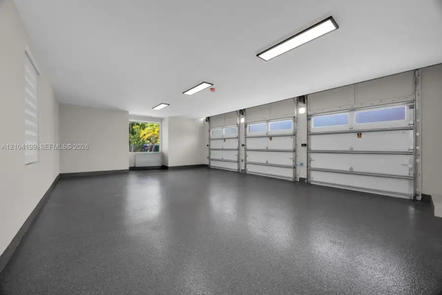 Three-car garage featuring a speckled epoxy-coated floor, bright LED panel lighting, and three sectional garage doors with frosted windows