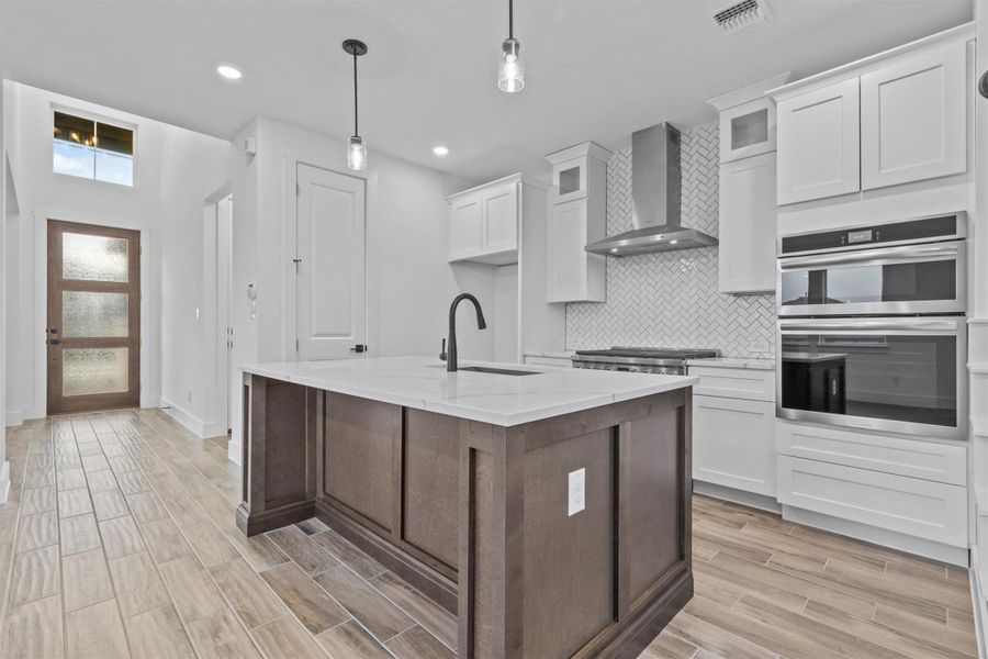 Kitchen with pendant lighting, appliances with stainless steel finishes, white cabinets, wall chimney range hood, and sink