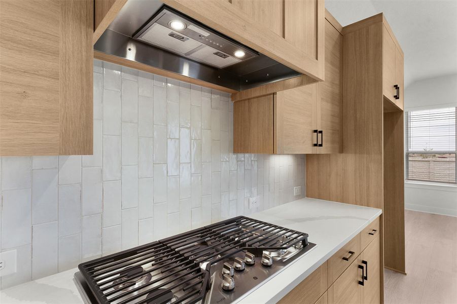 Kitchen with premium range hood, stainless steel gas cooktop, decorative backsplash, and light stone counters Kitchen with premium range hood, stainless steel gas cooktop, decorative backsplash, and light stone counters