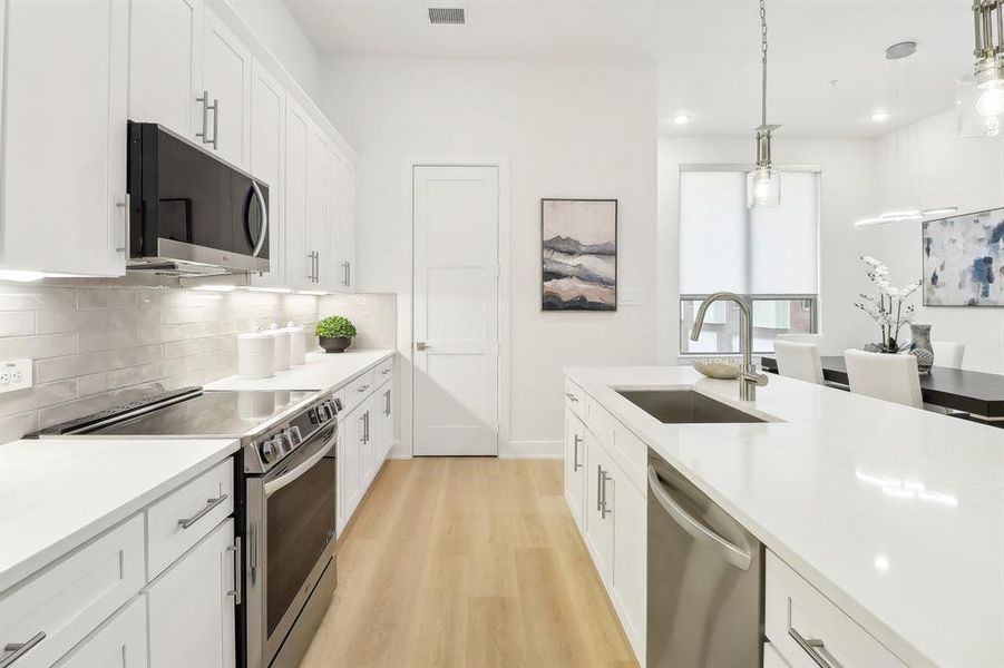 Kitchen featuring light wood finished floors, stainless steel appliances, tasteful backsplash, white cabinets, and a sink