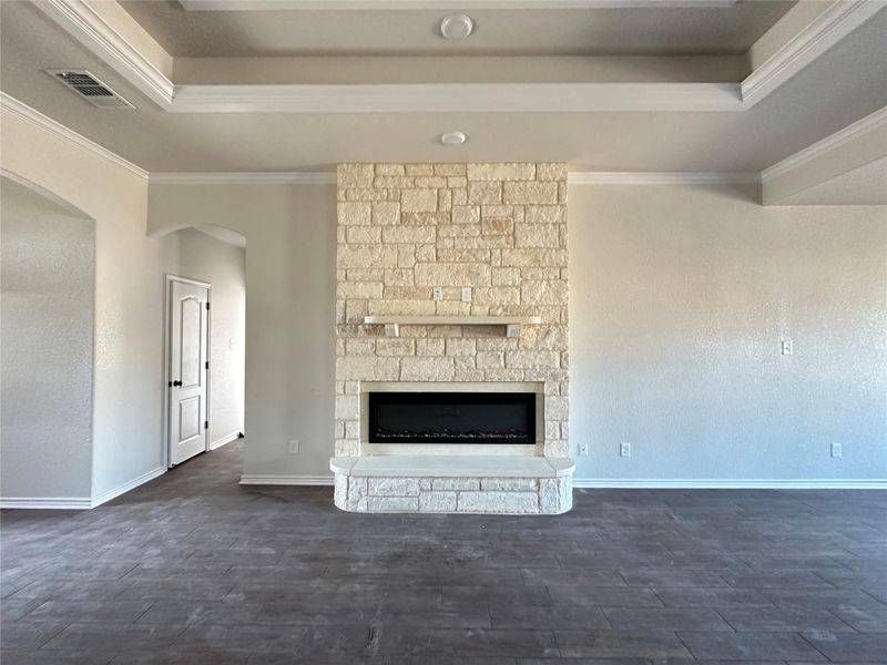 Unfurnished living room with arched walkways, a stone fireplace, dark wood-type flooring, ornamental molding, and a raised ceiling