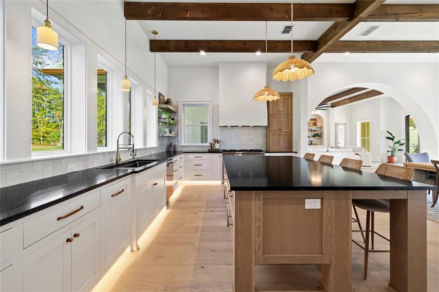 Kitchen with beamed ceiling, a breakfast bar area, tasteful backsplash, arched walkways, and decorative light fixtures